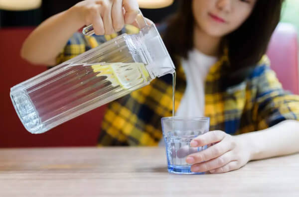 Жінка наливає у склянку воду з лимоном