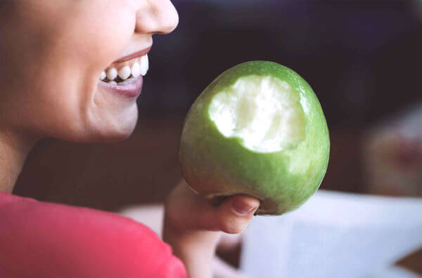 Дівчина з гарною посмішкою їсть яблуко