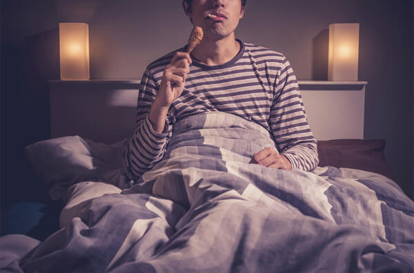 Чоловік їсть курячу ніжку у ліжку