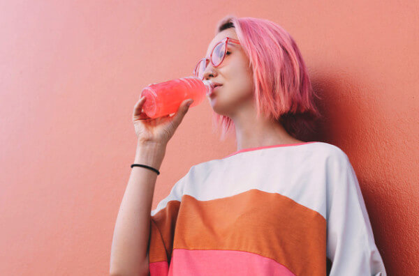 Жінка з рожевим волоссям п'є рожевий напій