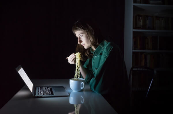 Жінка їсть локшину перед екраном комп'ютера