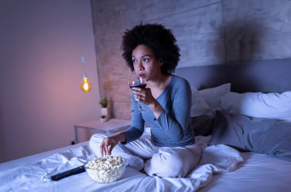 Жінка їсть попкорн і п'є вино у ліжку